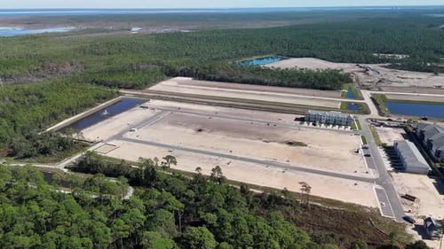 A Growing Neighborhood Featuring Land Plots, Buildings, and a Retention Pond, Surrounded by Greenery