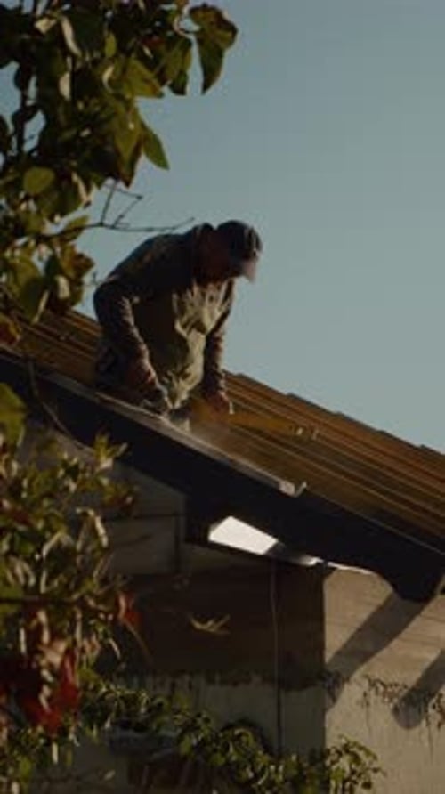 Vertical video Worker installs roofing on a house under a clear sky