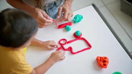 Close up shot of a brunette boy with his mom creating a truck figure out of red and blue play dough