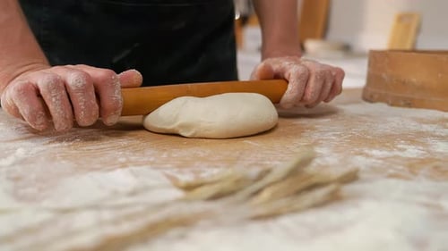 Person Rolls Dough on Floured Wood Surface