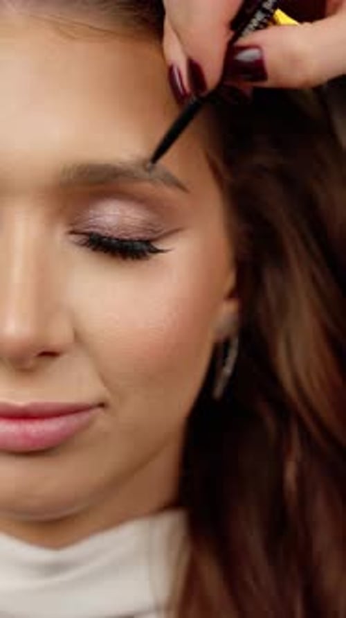 Professional Makeup Artist Grooming Model's Eyebrows Meticulously Defining Facial Contours with