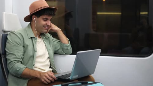 Entspannter Reisender mit Kopfhörern und Laptop im Zug auf dem Weg zu seinem Urlaubsort, 4K-Video