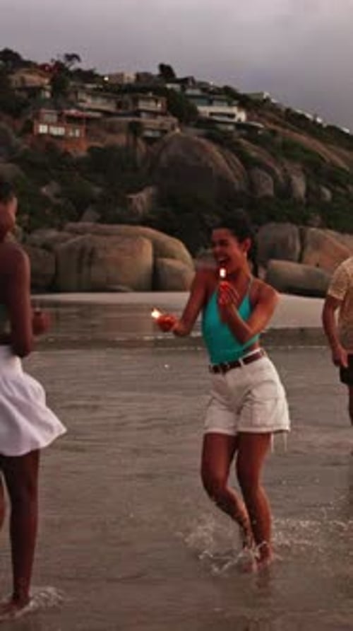 Sparklers, excited and group of friends by beach for summer vacation, getaway