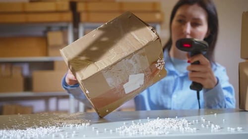 Ein beschädigtes Paket, eine kaputte weibliche Box, wird von einem Lagerarbeiter mit einem Barcodescanner überprüft
