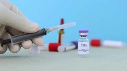 Hands taking syringe and verifying and choosing the dengue vaccine from table at hospital.