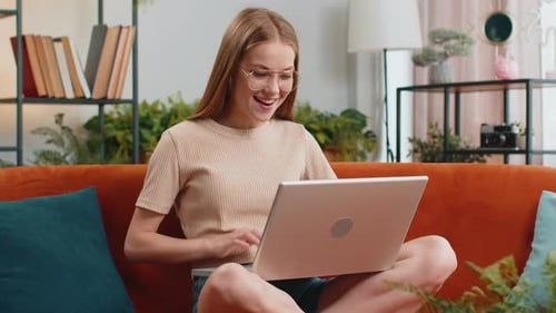 Woman works at laptop and celebrates on couch