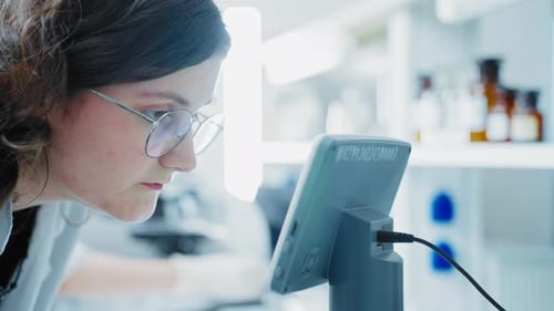 Young Scientist Examining Data on Microscope Tablet
