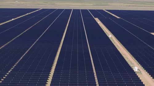 Large solar panel farm in a remote area with clear skies and long rows, aerial view