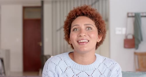 Expressing surprise, woman with curly hair gesturing with hand indoors, video call