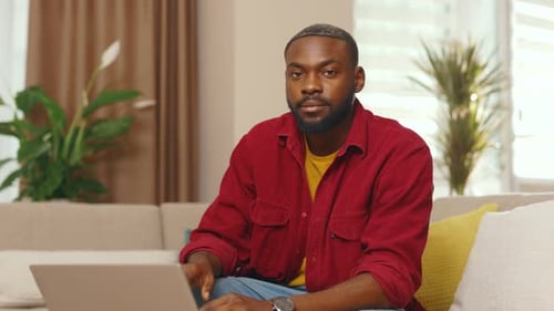 Man Smiling, Sitting With Laptop on Couch Indoors