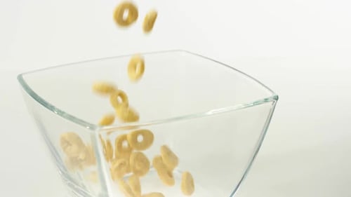 Yellow cereals fall in a transparent square bowl on a white background. Healthy breakfast meal