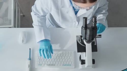 Scientist Using Microscope and Typing in Lab