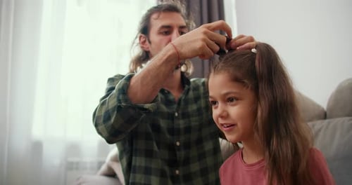 A Brunette Guy with Long Hair in a Green Checkered Shirt Gives His Little Daughter in a Pink Jacket