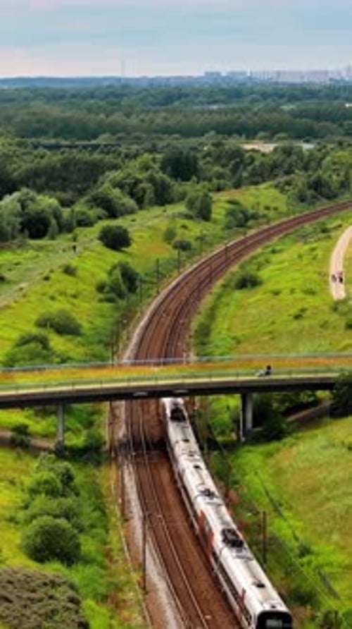 Aerial drone view of a train moving on the rails towards a city. Vertical