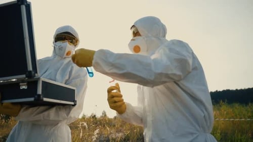 Scientists Wearing Protective Gear Diligently Collecting Crucial Samples in the Field for Analysis