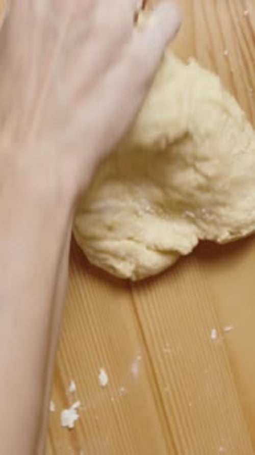 Vertikales Video. Ansicht von oben, während die Frau hinter einem Holztisch den Teig von Hand knetet
.