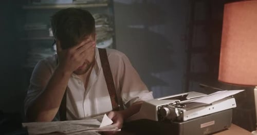 Young Writer Concentrating on a New Short Story Sitting at a Table in a Dark Smoky Office