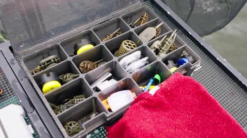 Nahaufnahmebox mit Angelködern, Schnüren und Haken am Pier am Flussufer, Natur, Sportfischen