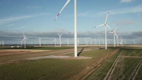 Drone is heading towards the trunk of a wind mill. low view on a row of wind mills. Blades are spinn