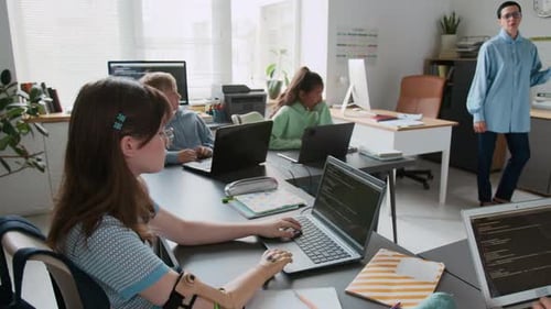 Girl with Prosthetic Arm Typing Code on Laptop During Group Programming Lesson