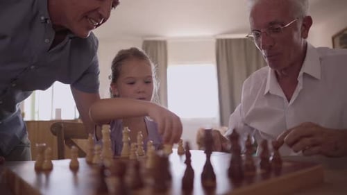 Joyful multi generational family playing a chess board game at home, with the grandfather teaching h