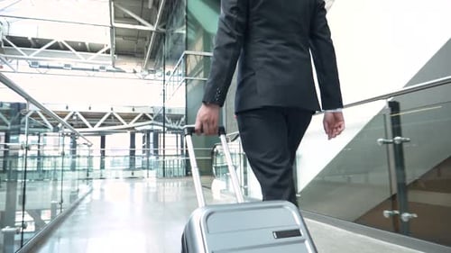 Businessman walking pulling suitcase through bright airport atrium