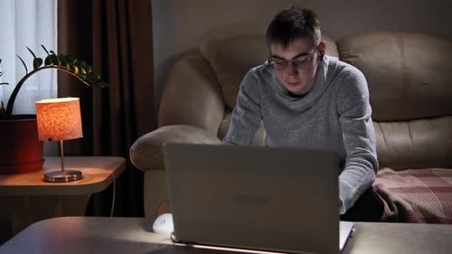 Im Wohnzimmer sitzt der Student auf einem Sofa in der Nähe des Fensters und arbeitet an seinem Laptop