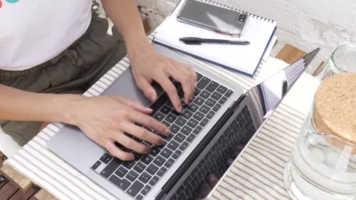 Frau mit Blick von oben, die an ihrem Laptop arbeitet und draußen an einem Cafétisch auf einer Tastatur tippt