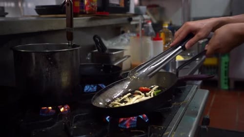 Professional chef flipping the ingredients in the frying pan and mixing with a tongs, cooking delici