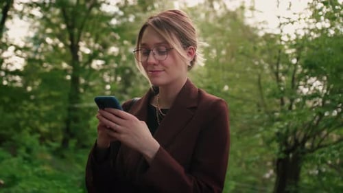 Woman Using Phone in the Park Caucasian Girl with Glasses Holding Mobile Phone outdoorsFemale