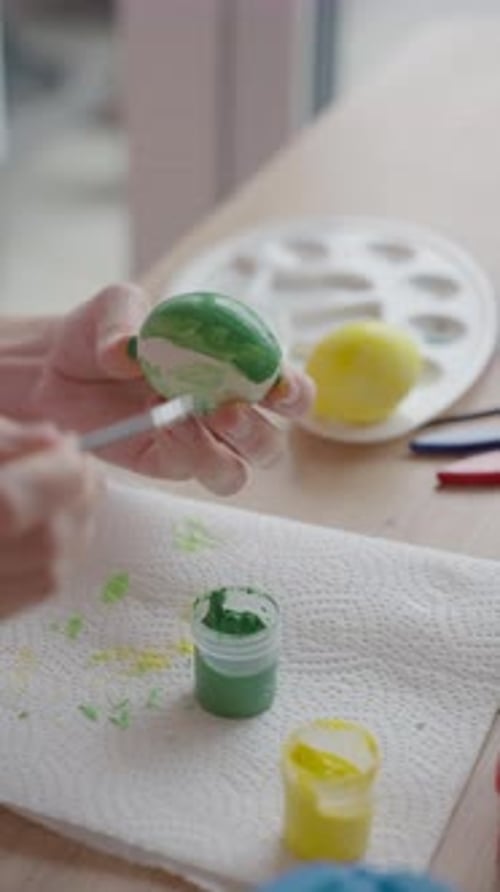 Woman painting Easter egg with green paint and brush