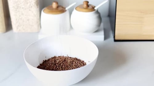 Buckwheat Groats Being Poured into a White Bowl