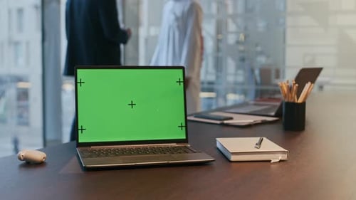 Laptop with Green Screen in Office with Businessmen Negotiating in Background