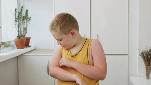 Boy Scratching his Arm in a Bright Kitchen