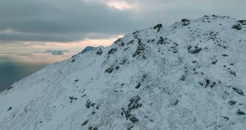 Orbiting frozen mountain peaks aerial view across Lofoten islands blue seascape at sunset
