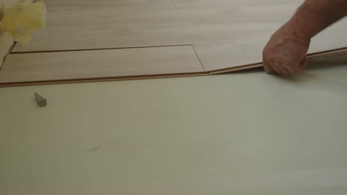 A Worker Carefully Lays Down Laminate Flooring in a Residential Space Ensuring Precise Placement The