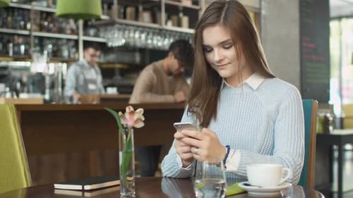 Attractive Young Woman using Mobile Phone at Cozy Coffee Shop.