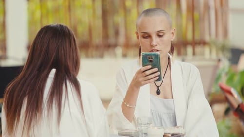 Two Women at a Table One Using Cellphone