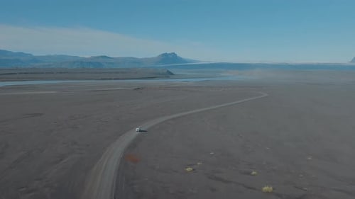 Aerial view of a white terrain car driving across the surreal Iceland desert. Black gravel land.