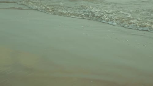 Ocean wave gently rolling onto a sandy beach at the seashore, creating a calming foam pattern