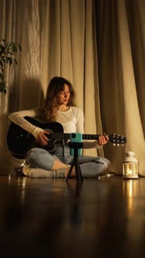 Woman Plays Guitar by Lantern Light at Home