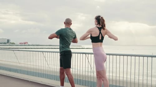 A young couple of athletes synchronously perform body turns, warming up before street workout