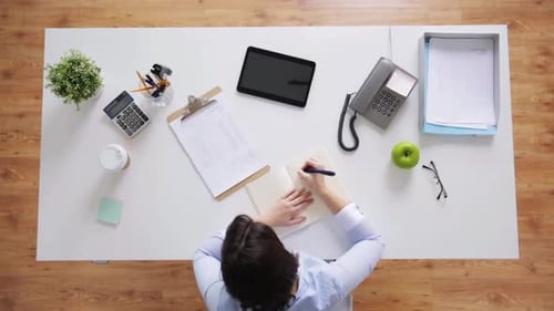 Young businesswoman taking notes at office desk in modern corporate workplace