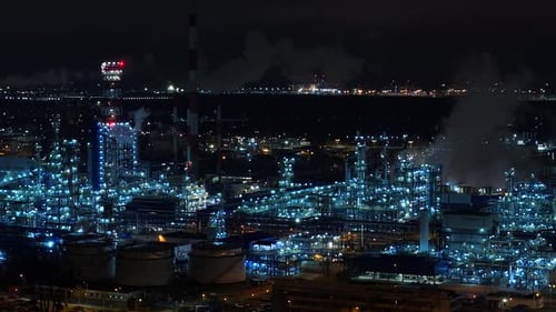 Oil refinery petrochemical plant illuminated at night with smoking chimneys