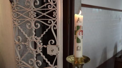 Decorated Paschal candle burning beside ornate metal grille inside church