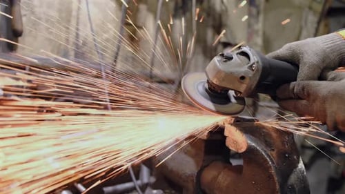 A worker in a workshop works with a circular saw. Sparks fly from hot metal.
