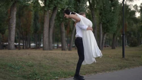 Groom Lifting Cheerful Bride in Wedding Dress During Playful Walk in Park