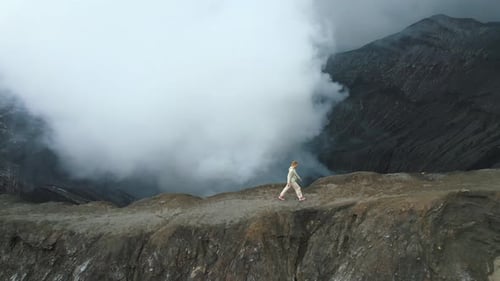 Aerial View of Woman Walks Along Edge of the Steaming Crater of Active Volcano