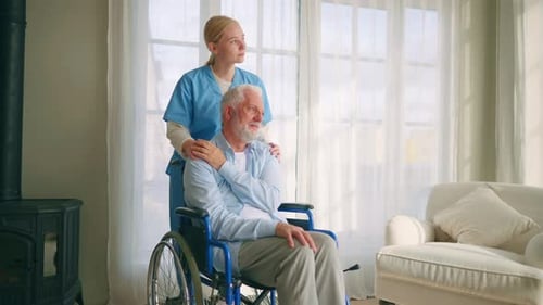 Caring Woman Supporting Senior Man in Wheelchair Indoors