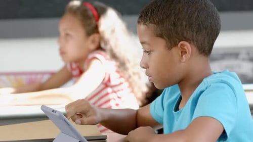 Biracial boy and girl focused on their tablets in the classroom at school